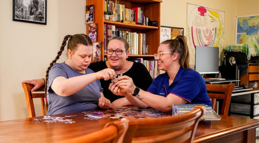 A mother and daughter sit down to do a puzzle with their HenderCare support worker.