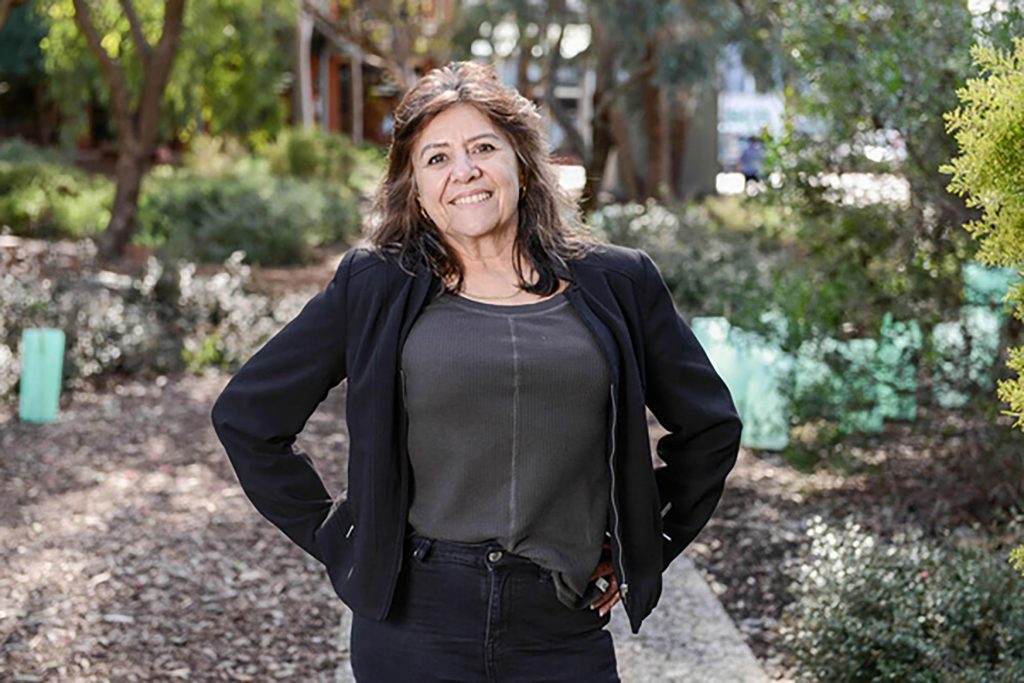 smiling lady with brown hair looks at camera with black jacket and grey pants